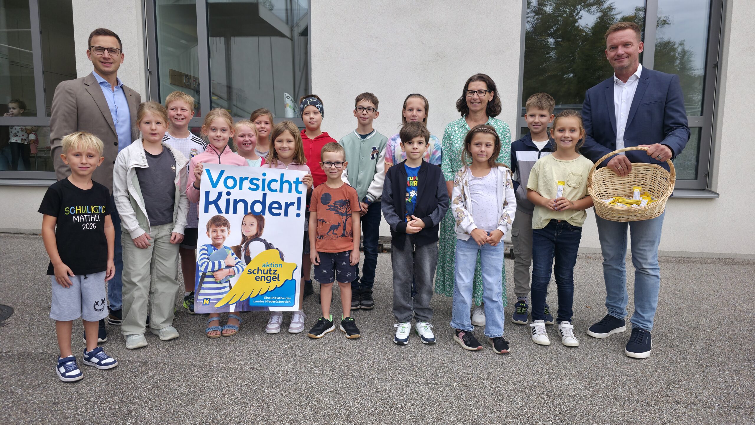 Schulkinder und Erwachsene mit Plakat "Vorsicht Kinder!" vor einem Gebäude in Niederösterreich